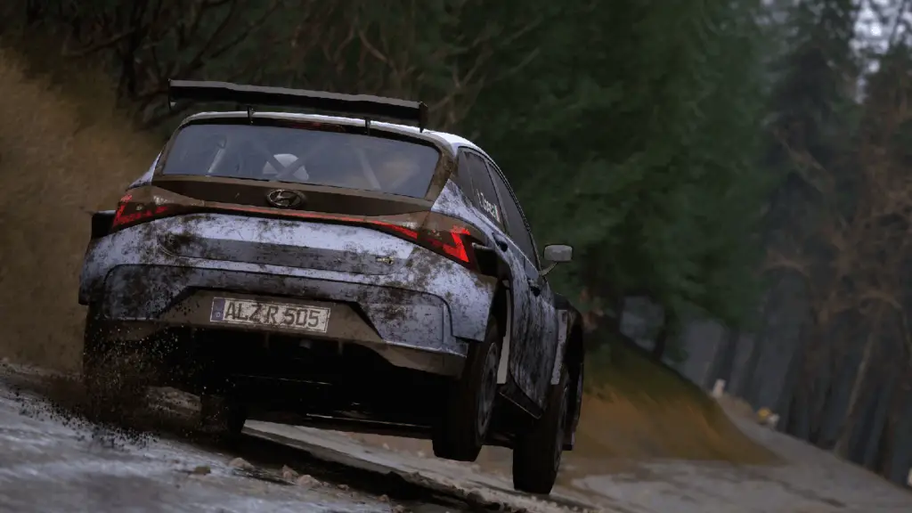 A rally car speeds down a muddy road, kicking up dirt, in Assetto Corsa Rally.