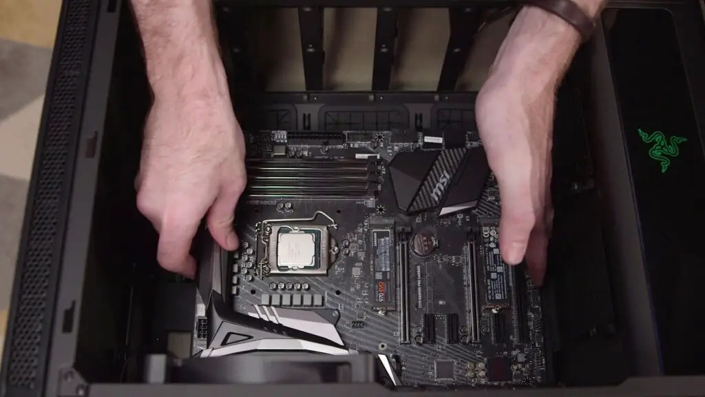 We see a pair of hands installing a motherboard inside of a PC case.