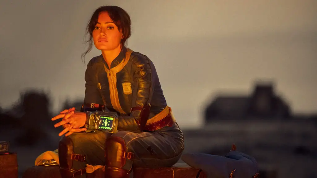 A character from the Fallout TV show, Lucy, looking determined and holding a weapon.