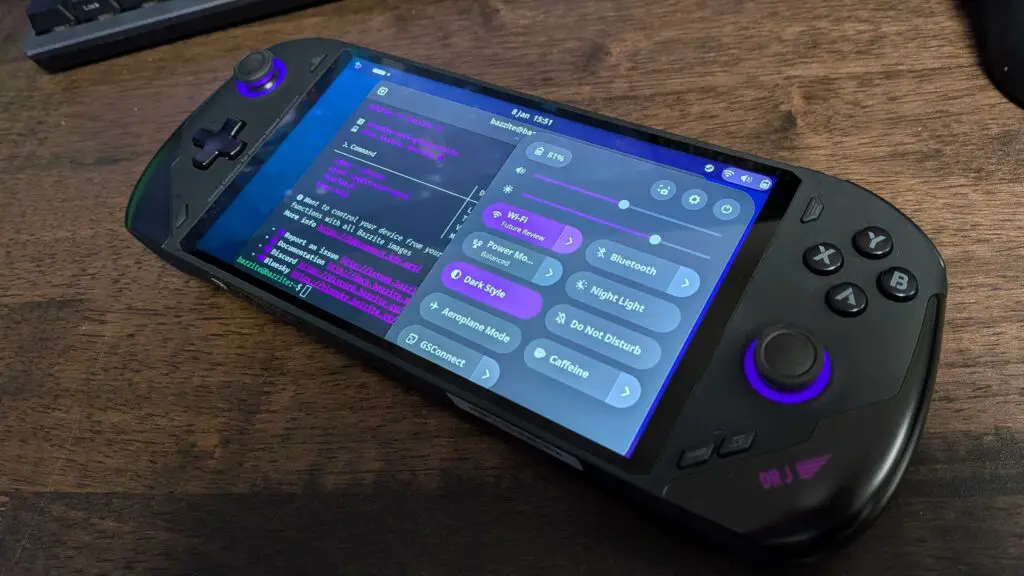 A handheld gaming PC on a desk running Bazzite, a Linux OS, on-screen.