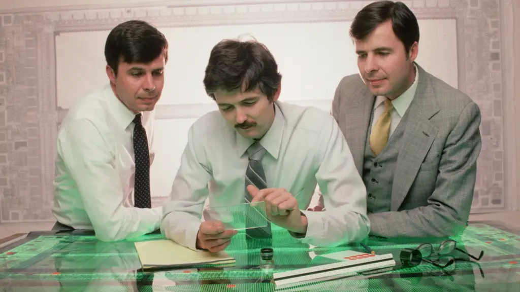 Twins Joe and Ward Parkinson, the founders of Micron Technology, Inc., examine a computer chip with designer Doug Pitman at their manufacturing company in Boise, Idaho.