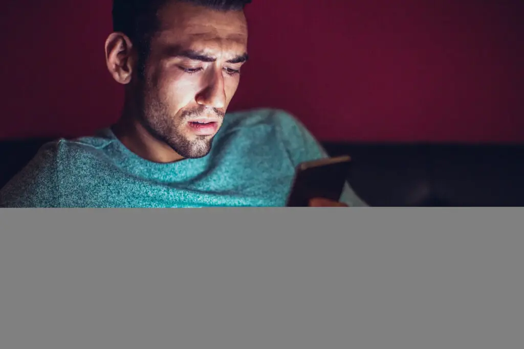 A man looking at a smartphone with a furrowed brow while sitting on a sofa.