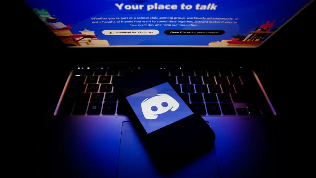Discord logo on a phone on top of a dark laptop.