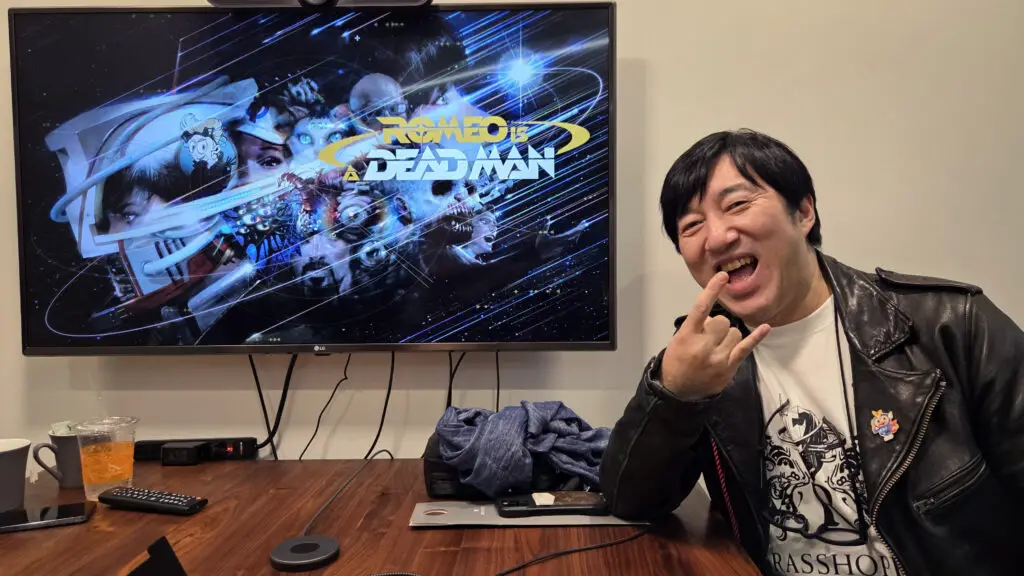 Suda51 posing in front of a TV showing Romeo Is a Dead Man
