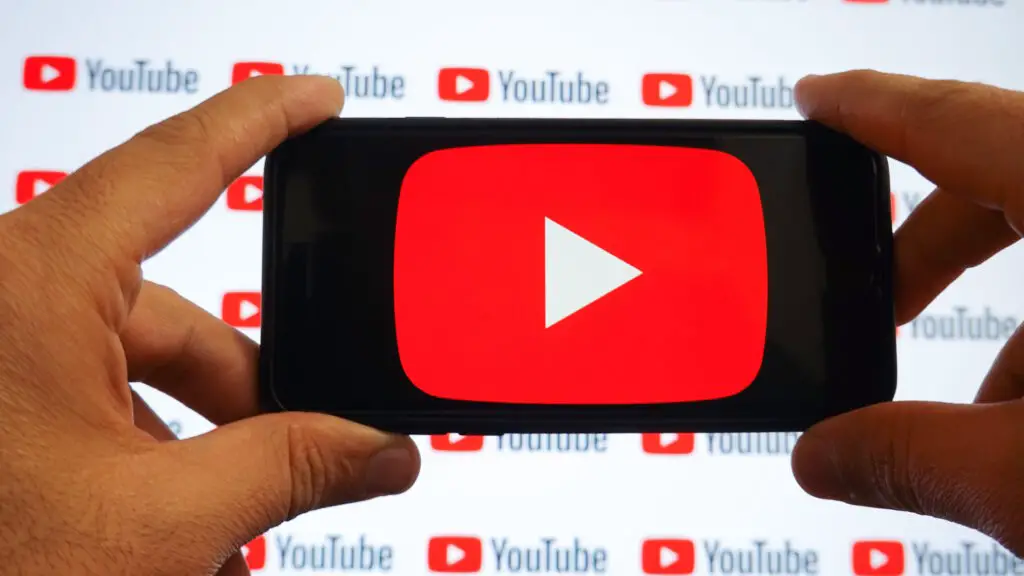 A man holding a smartphone with a Youtube logo and small YouTube logos displayed on a screen