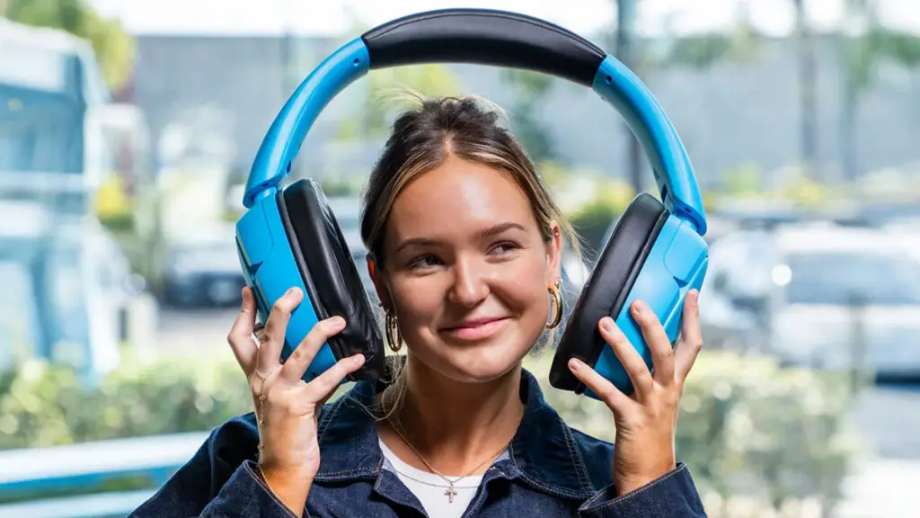 A comically huge set of blue headphones, being held on either side of a model's head