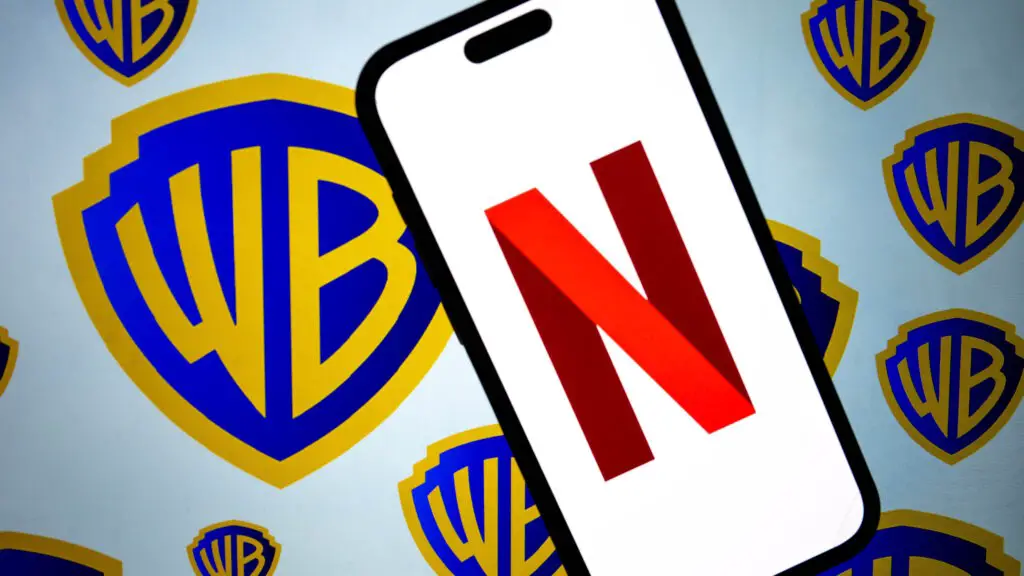 A photo illustration showing the Netflix logo displayed on a mobile phone screen in front of the Warner Bros logo.
